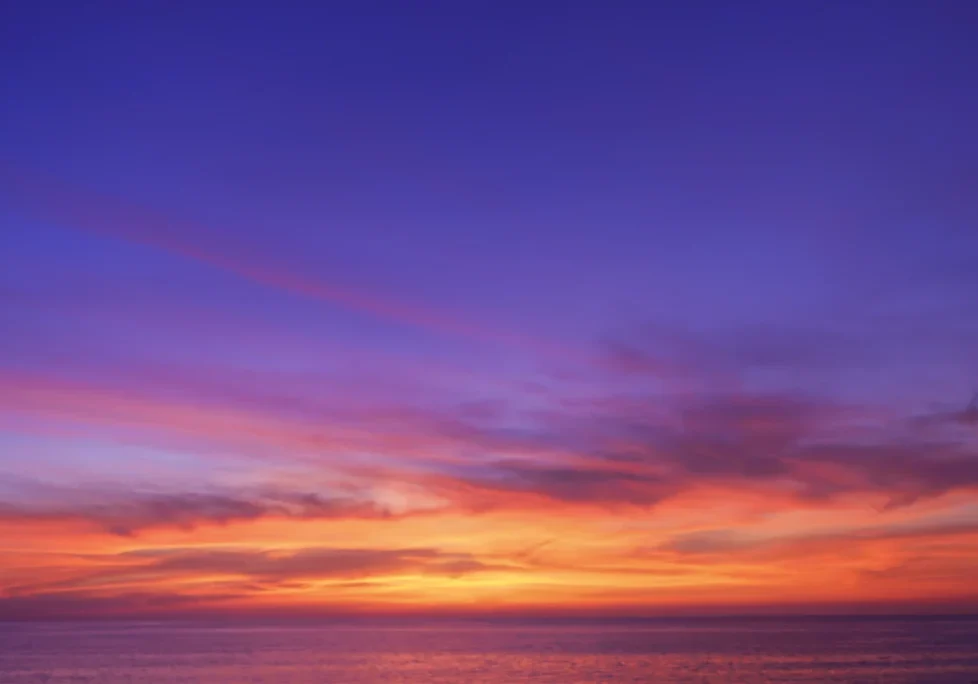 A sunset over the ocean with purple and orange clouds.